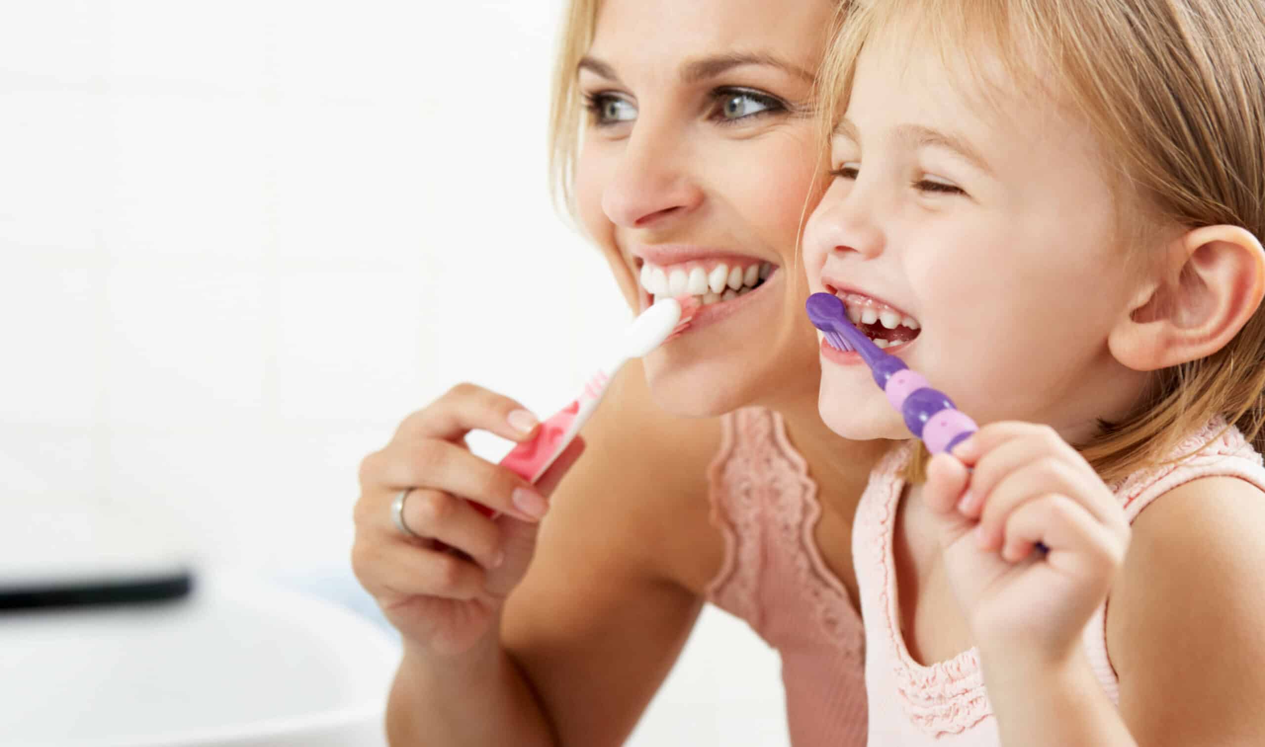 A person and a child are smiling while brushing their teeth together in a bright bathroom, creating a joyful and healthy atmosphere.