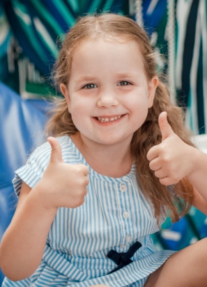 A smiling child in a striped dress gives a double thumbs-up gesture, with a blue and green patterned background. No landmarks or historical buildings visible.