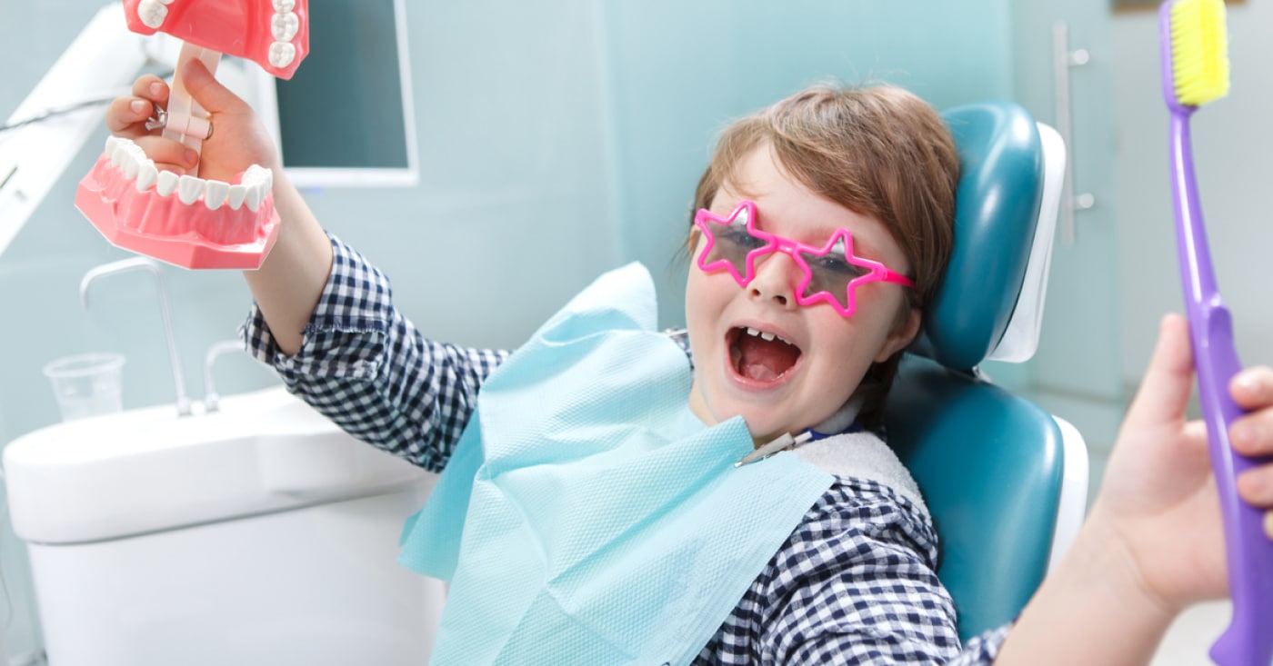 Smiling kid in dentist office chair with pink-star-shaped-dental glasses.