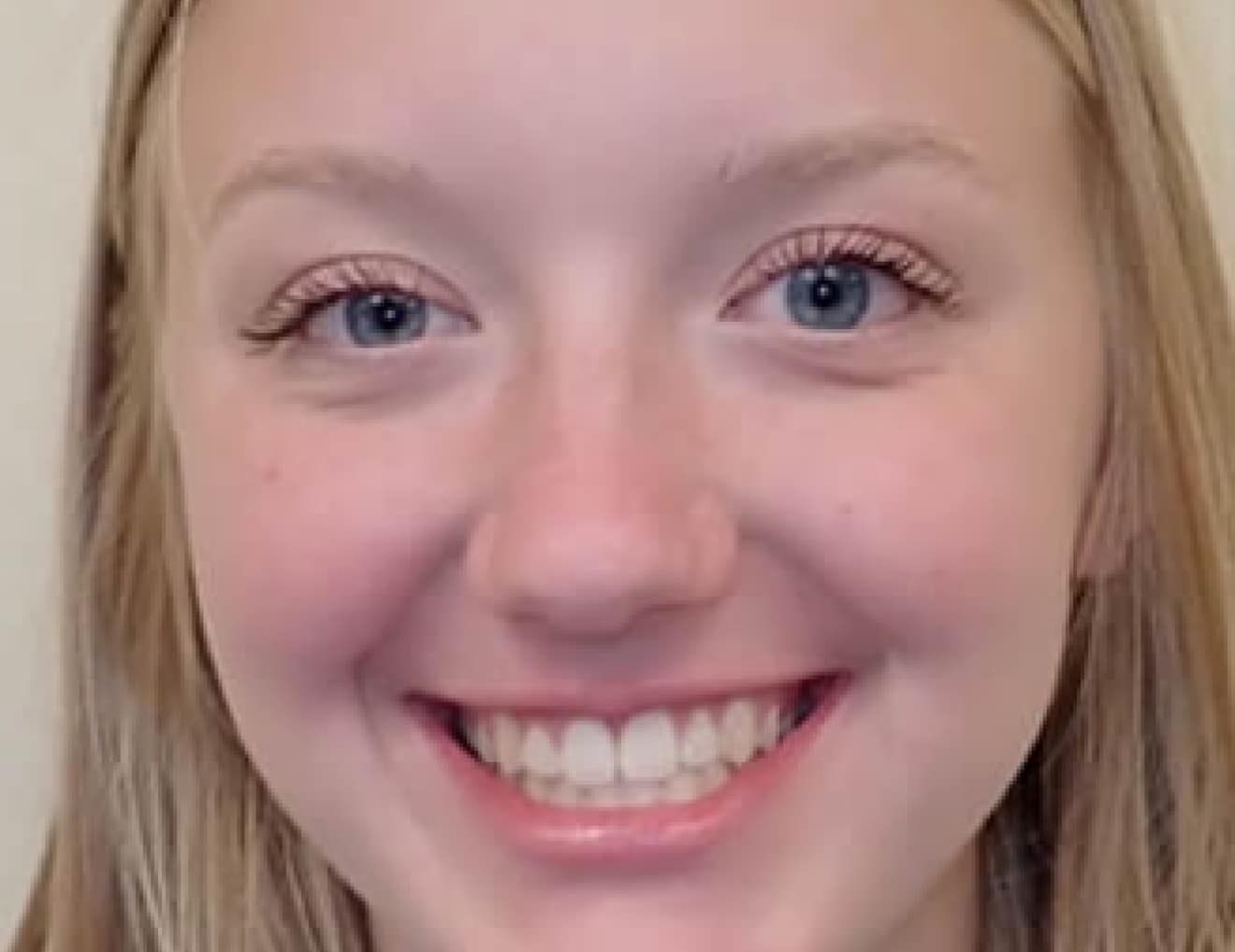 A close-up image of a smiling person with long, blonde hair and blue eyes. There are no visible landmarks or historical buildings.