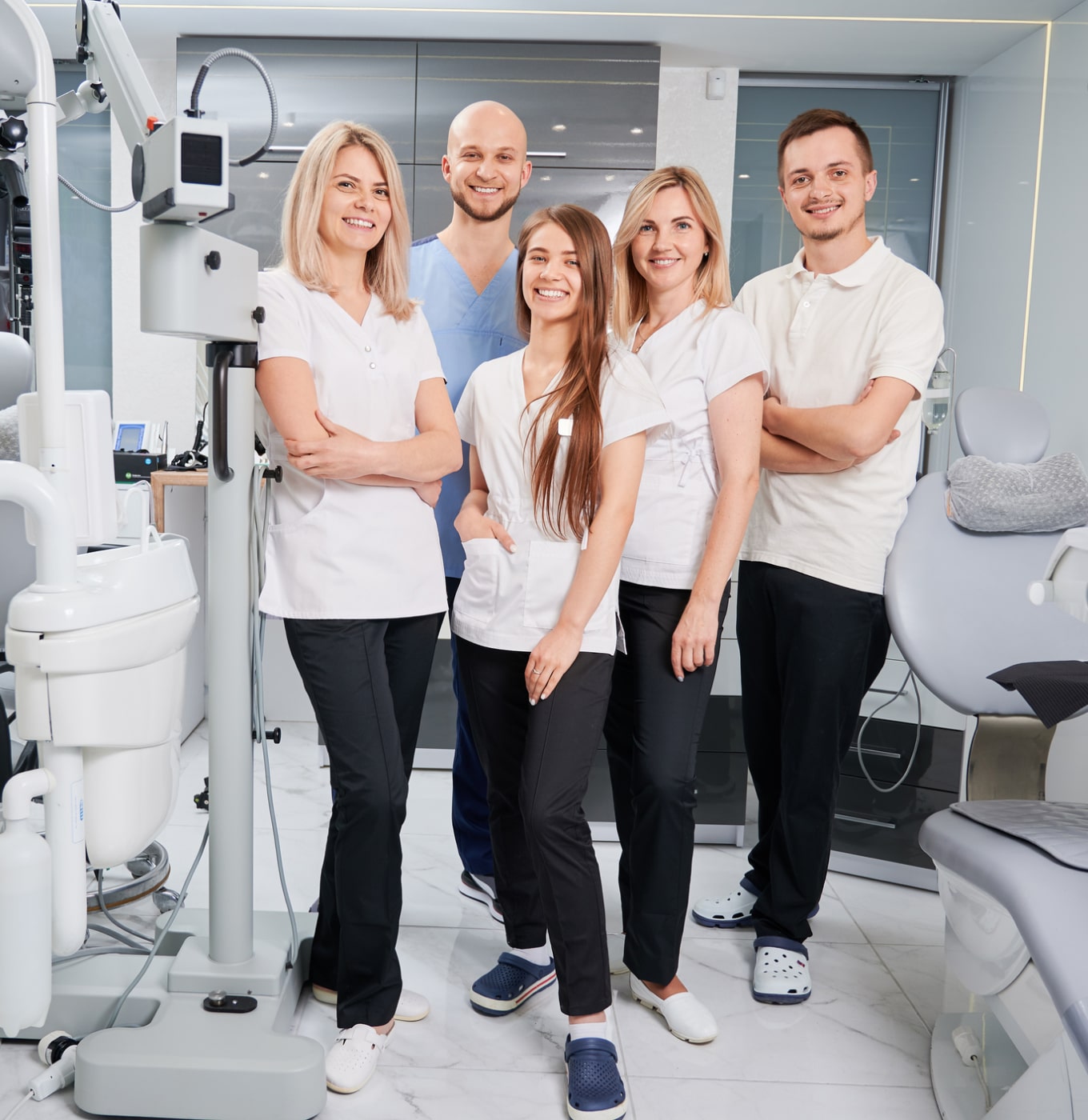 A group of five people dressed in medical attire stands in a modern dental office with equipment visible in the background.